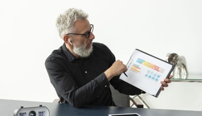 older-man-home-showing-graph-notepad-with-tablet-desk